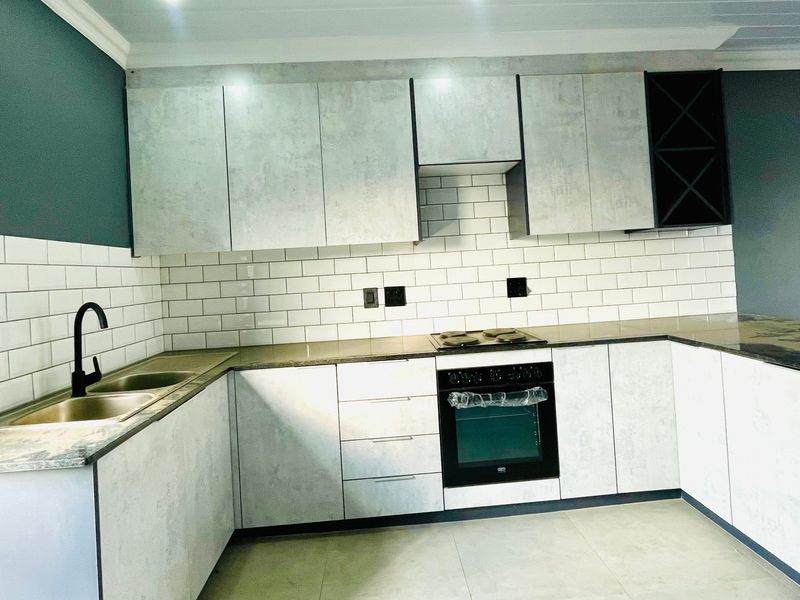 Modern kitchen featuring light grey cabinetry, subway tile backsplash, stone countertops, and integrated oven with electric hob.