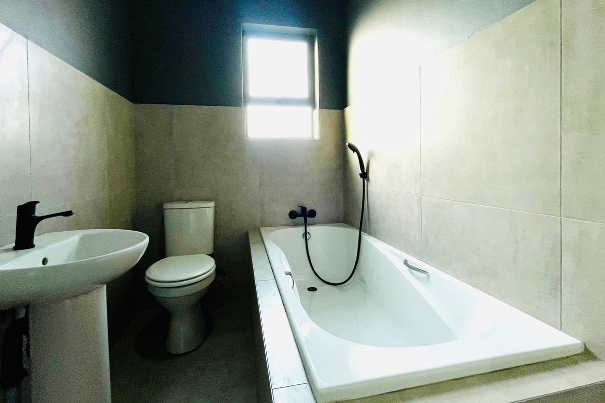 A modern bathroom featuring a pedestal basin, a standard toilet, and a built-in bathtub with a handheld shower mixer, finished with neutral wall tiles.