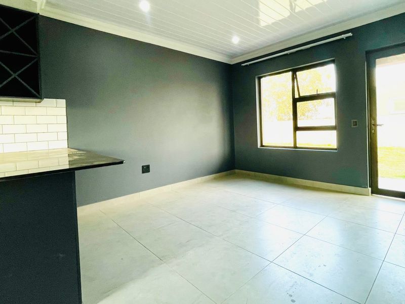 Modern open-plan living area featuring tiled floors, dark cabinetry with granite countertops, subway tile backsplash, and direct access to the garden through a glass door.