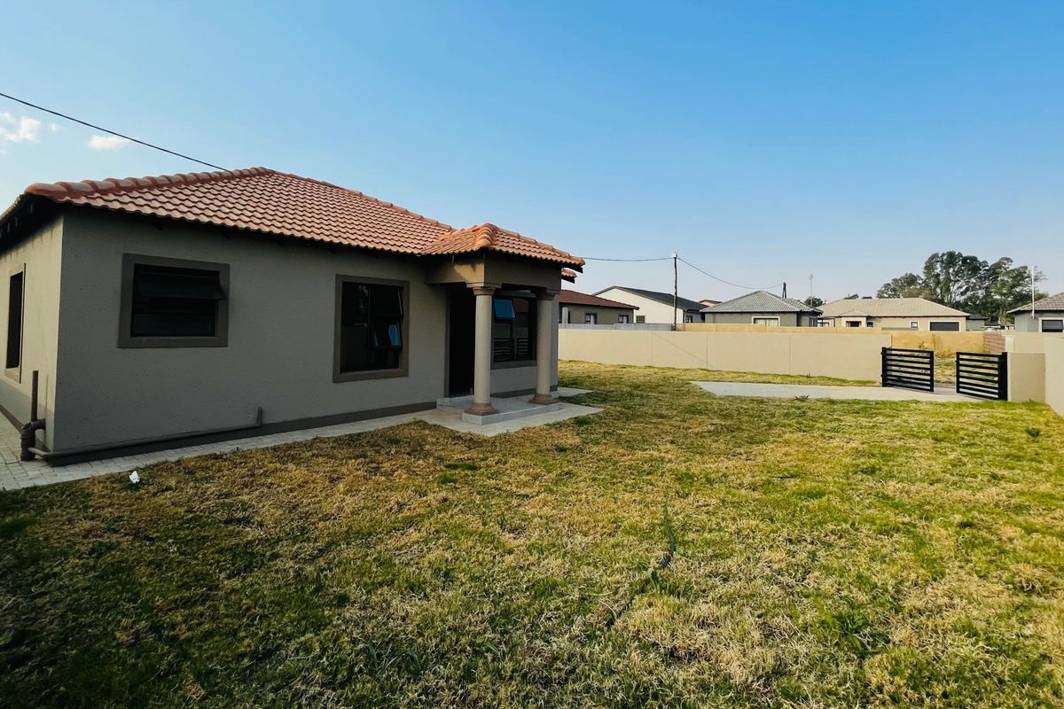 Rear view of a townhouse featuring a terracotta tiled roof, covered entrance porch with concrete columns, and a spacious backyard with perimeter walling.