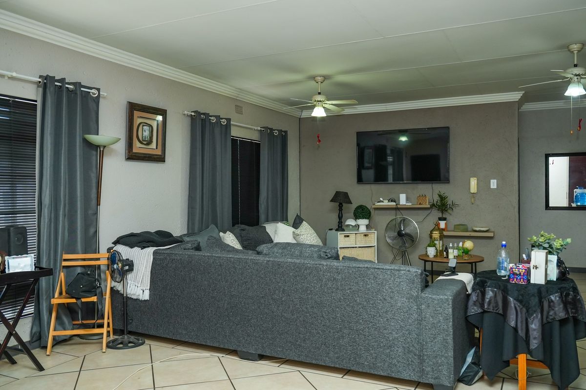 A spacious living room featuring tiled flooring, ceiling fans, and neutral wall tones, providing a functional and comfortable area for relaxation.