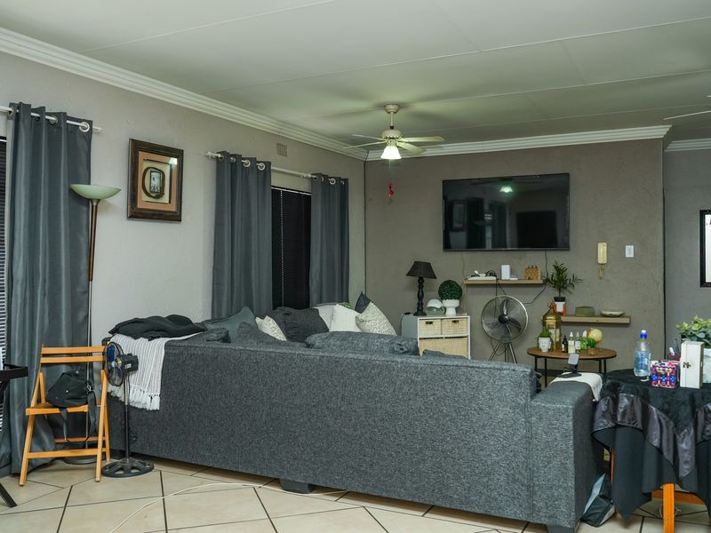 A spacious living room featuring tiled flooring, ceiling fans, and neutral wall tones, providing a functional and comfortable area for relaxation.
