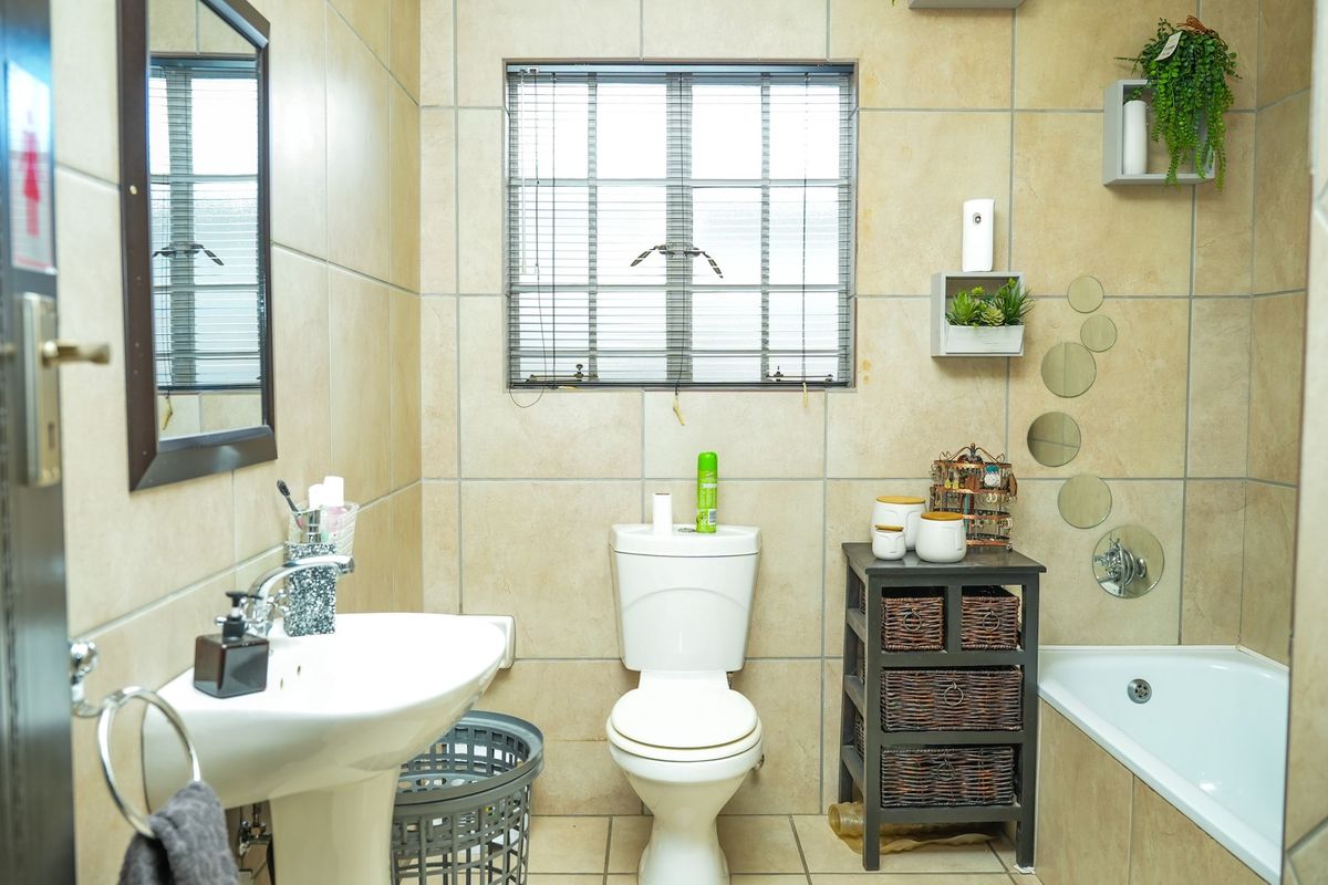 A functional bathroom featuring a pedestal basin, toilet, and bathtub with neutral wall and floor tiling.