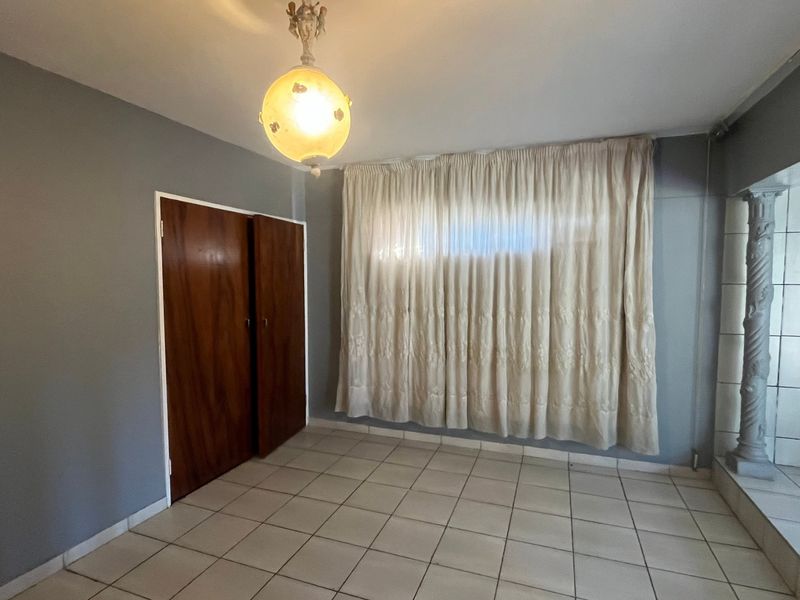 An empty bedroom featuring tiled flooring, built-in wooden cupboards, and a decorative pillar, offering a blank canvas for personalization.