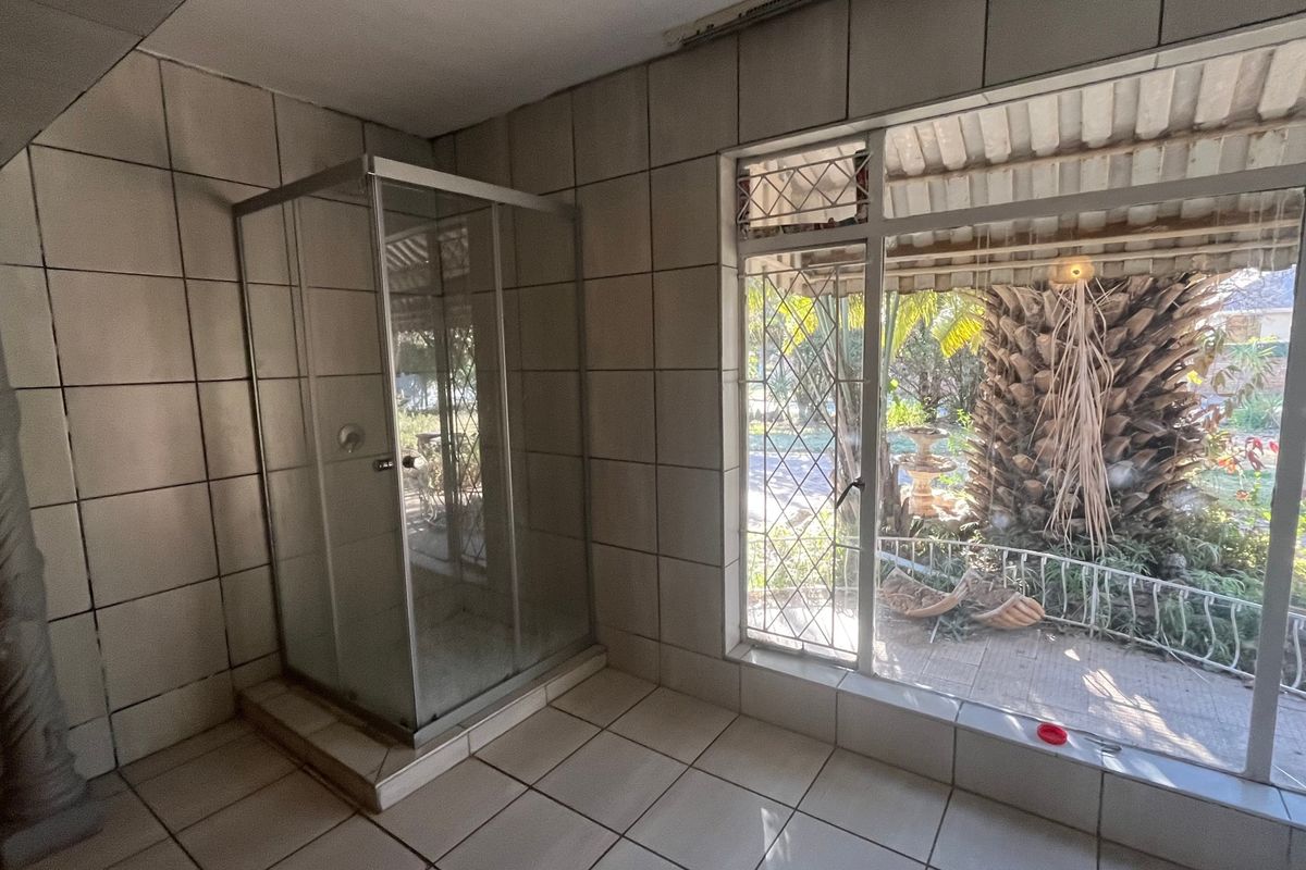 A spacious bathroom featuring a glass shower enclosure, fully tiled surfaces, and a large window providing natural light and garden views.