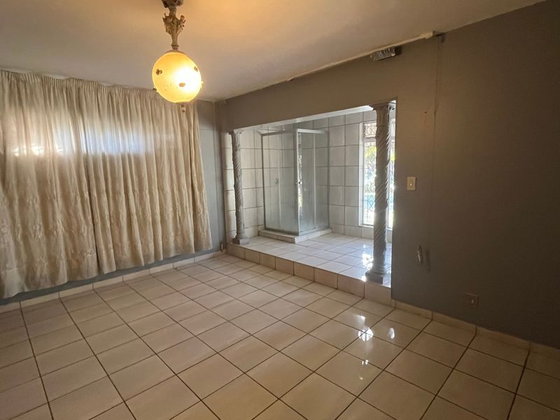 An empty bedroom featuring tiled flooring, a raised platform area with an integrated shower enclosure, and decorative columns.