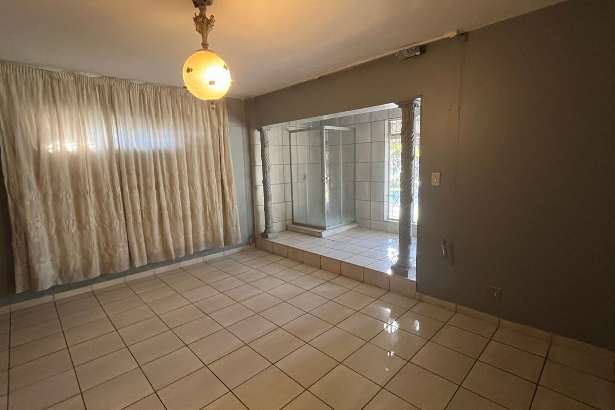 An empty bedroom featuring tiled flooring, a raised platform area with an integrated shower enclosure, and decorative columns.