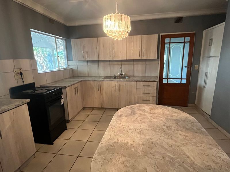 A functional kitchen featuring light wood-look cabinetry, stone-patterned countertops, tiled flooring, and a freestanding stove, offering a practical layout with ample storage space.