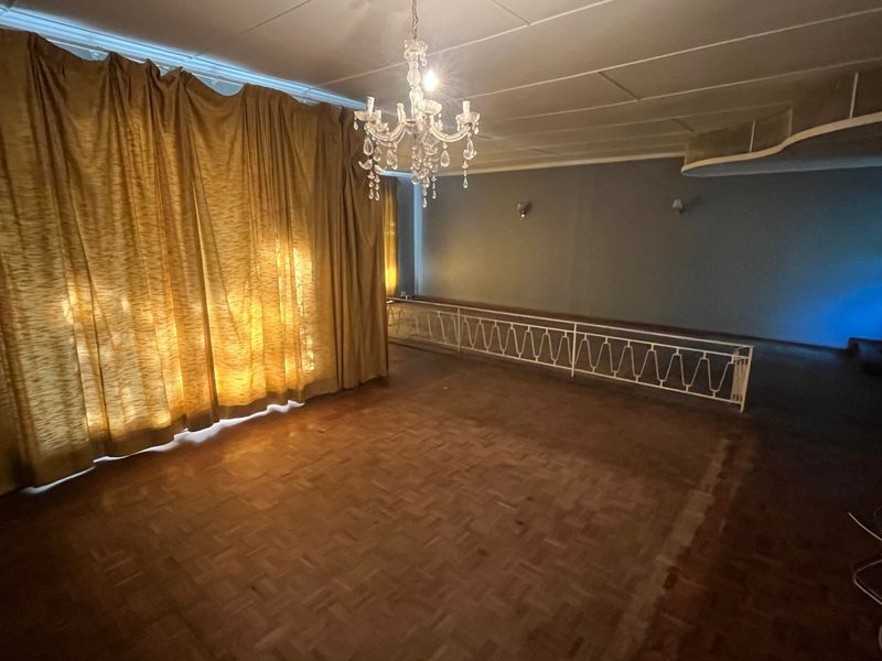 Spacious living area featuring original parquet flooring, a decorative metal balustrade, and a classic crystal chandelier, offering a versatile blank canvas for renovation.