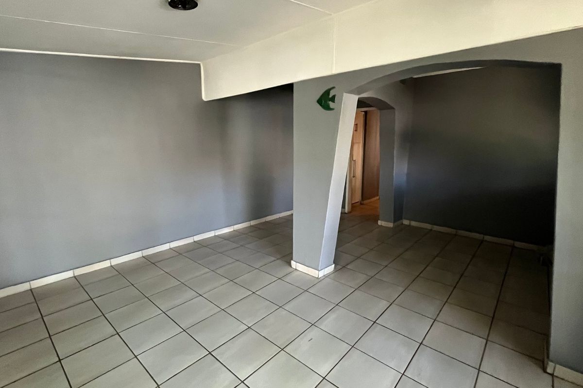 An empty living area featuring neutral grey walls, tiled flooring, and a distinctive arched architectural opening leading to an adjacent space.