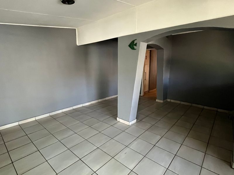 An empty living area featuring neutral grey walls, tiled flooring, and a distinctive arched architectural opening leading to an adjacent space.