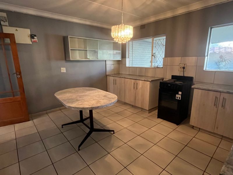 A functional kitchen featuring tiled flooring, built-in cabinetry with laminate countertops, a tiled backsplash, and a freestanding stove.