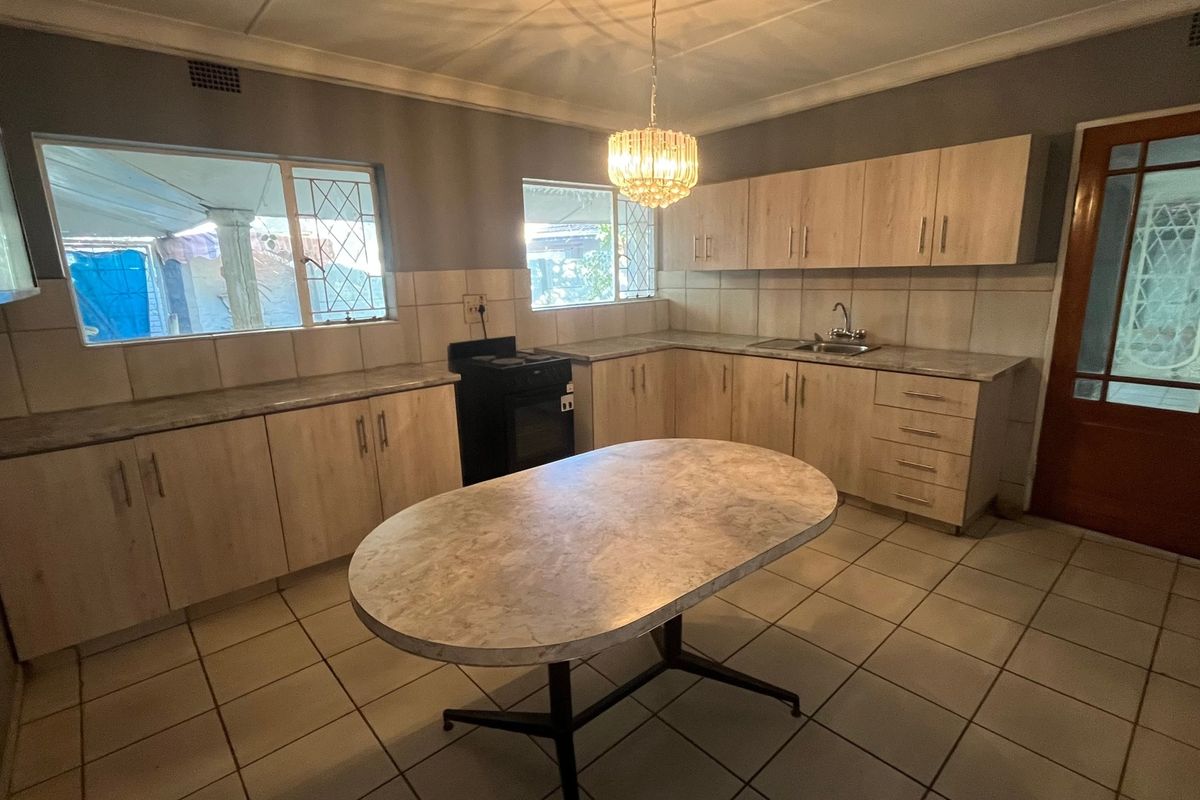 A functional kitchen featuring light wood-look cabinetry, laminate countertops, tiled flooring, and a central dining island, offering a clean and practical workspace.