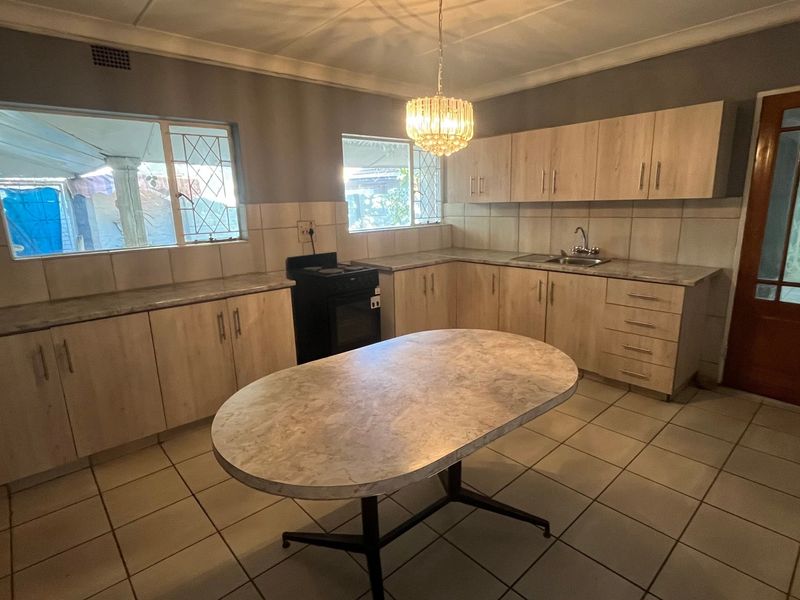 A functional kitchen featuring light wood-look cabinetry, laminate countertops, tiled flooring, and a central dining island, offering a clean and practical workspace.