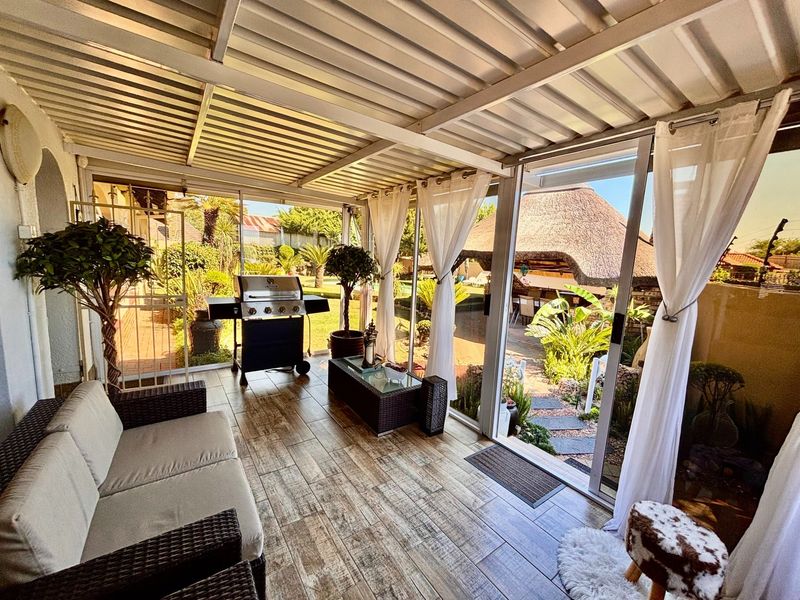 A covered patio area featuring tiled flooring, a corrugated metal roof, and sliding glass doors that open out to a landscaped garden.