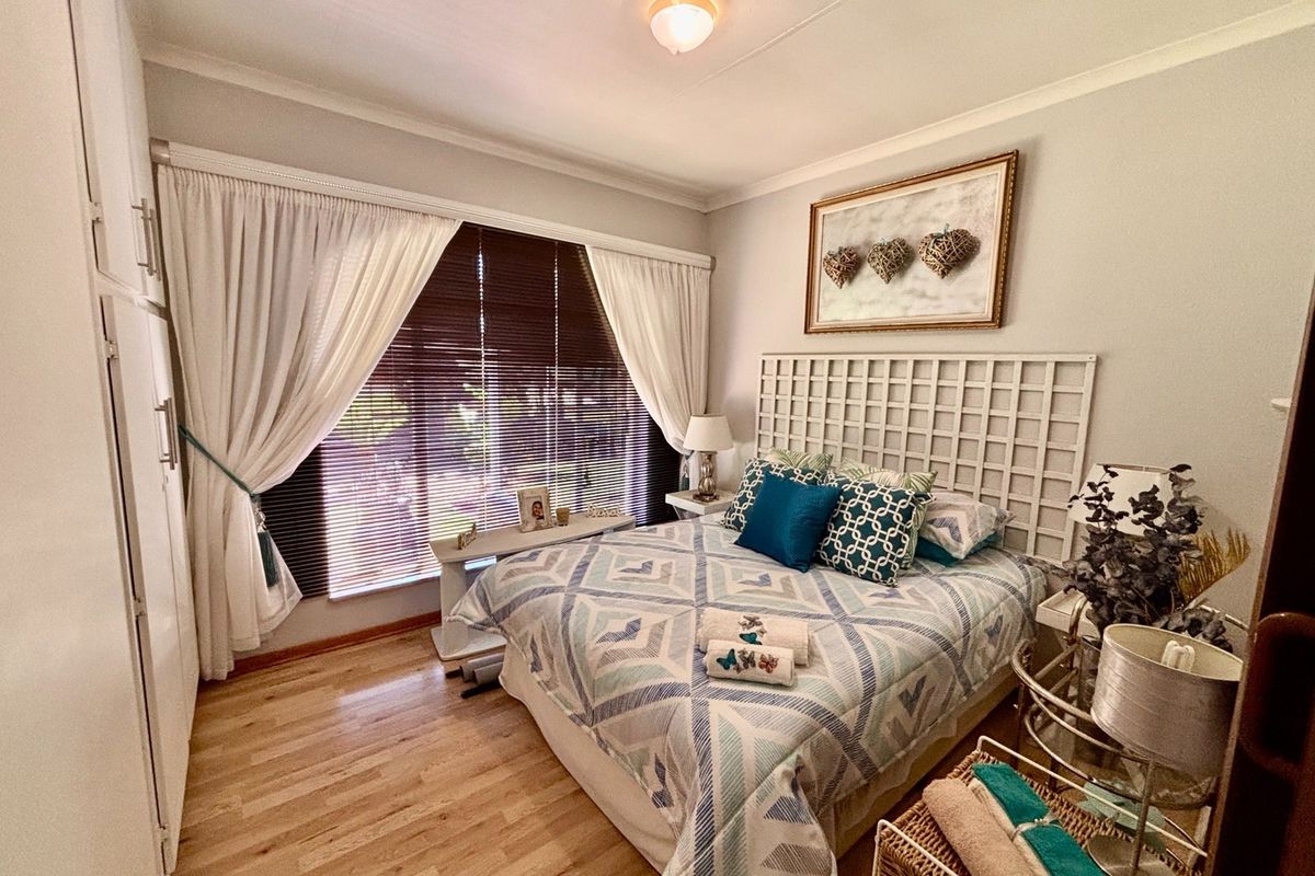 A well-maintained bedroom featuring light wooden flooring, built-in cupboards, and large windows with venetian blinds, offering a bright and comfortable living space.