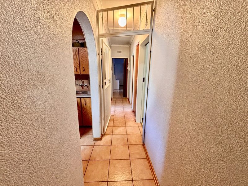 A functional hallway featuring tiled flooring, an arched entryway, and a security gate, providing access to adjacent rooms within the home.