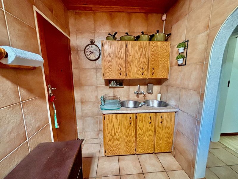 A functional scullery area featuring wooden cabinetry, a double basin sink, tiled walls, and a timber ceiling.