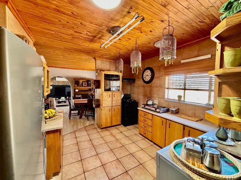 A functional kitchen featuring wooden cabinetry, tiled flooring, a built-in oven, and a warm wooden ceiling, with an open-plan flow to the dining area.