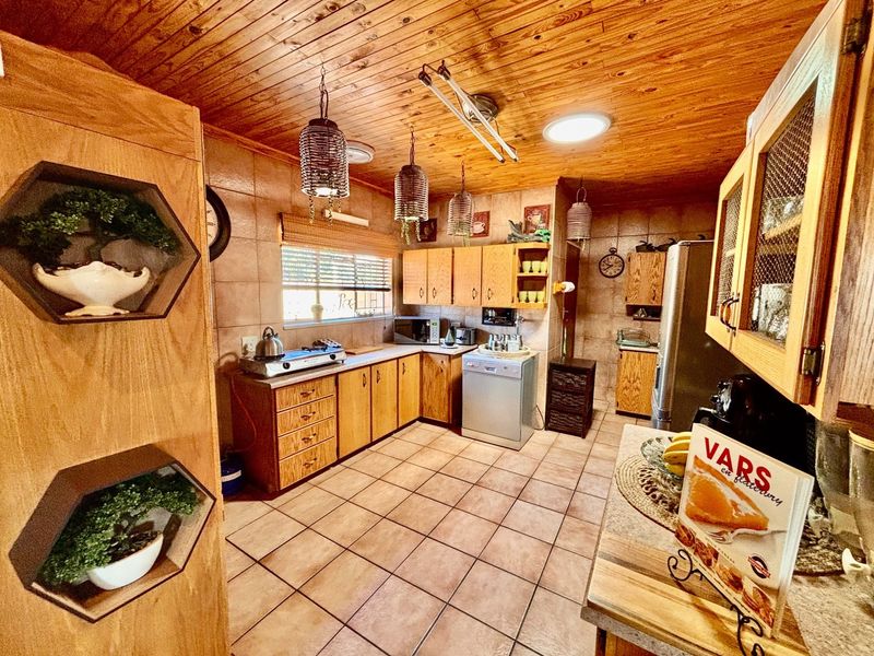 A functional kitchen featuring wooden cabinetry, tiled flooring, and a timber-clad ceiling, offering a traditional aesthetic with integrated appliance space.