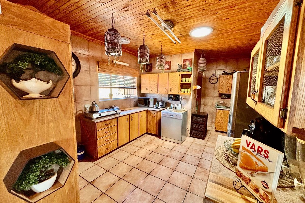 A functional kitchen featuring wooden cabinetry, tiled flooring, and a timber-clad ceiling, offering a traditional aesthetic with integrated appliance space.