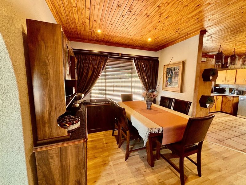 Open plan dining area featuring timber ceiling finishes and laminate flooring, flowing into an adjacent kitchen space with tiled floors.