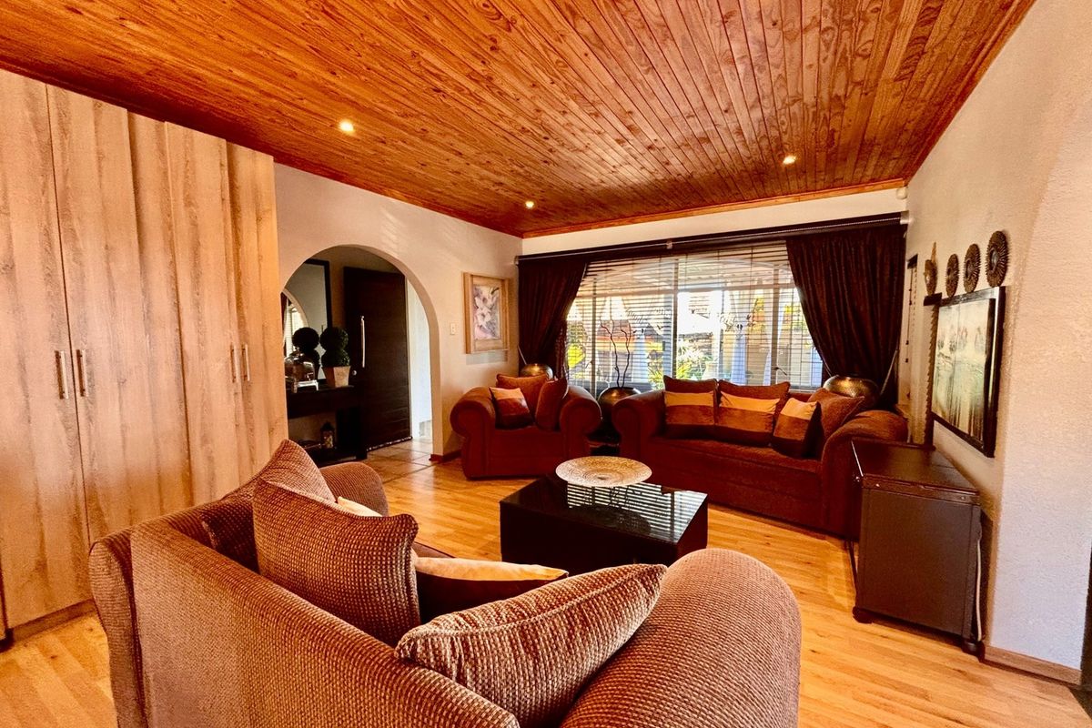 A cozy living room featuring a warm timber-clad ceiling, recessed lighting, laminate flooring, and a classic archway leading to the entrance.