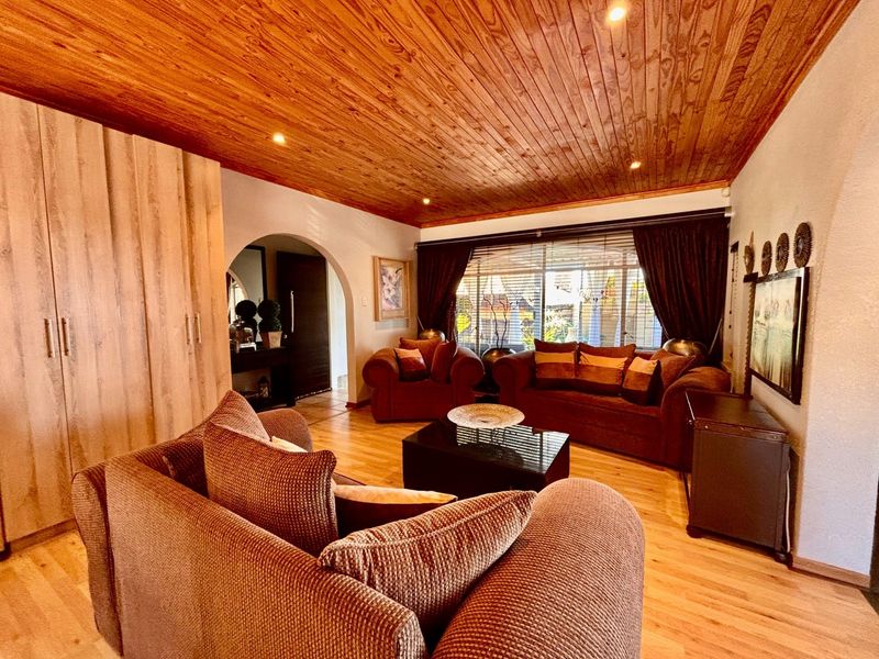 A cozy living room featuring a warm timber-clad ceiling, recessed lighting, laminate flooring, and a classic archway leading to the entrance.