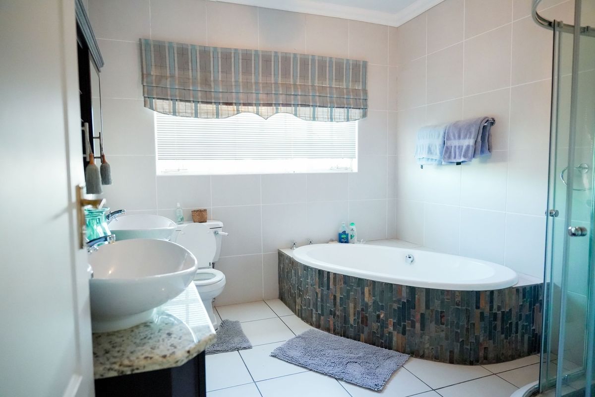 A well-maintained bathroom featuring a dual vanity with granite countertops, a stone-tiled built-in bathtub, and a separate glass-enclosed shower.