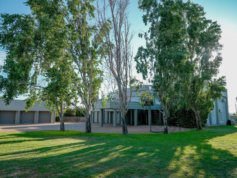 Front view of the farm property featuring a triple garage, paved driveway, and a covered entrance portico surrounded by mature trees and lawn.