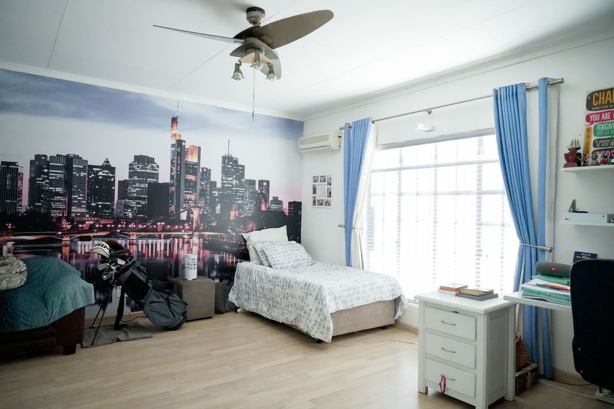 A spacious bedroom featuring laminate flooring, a ceiling fan, and a wall-mounted split-system air conditioner, offering a comfortable living space.