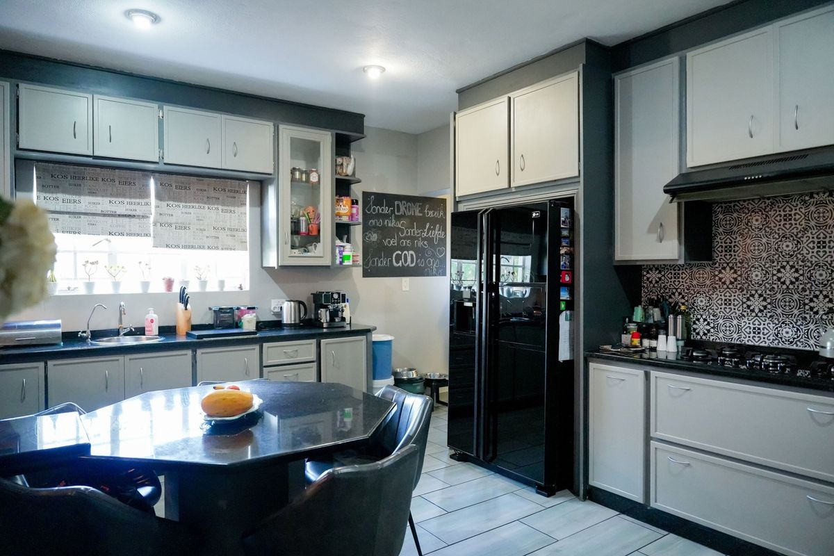 A well-maintained kitchen featuring modern grey cabinetry, granite countertops, a gas hob with extractor fan, and decorative tiled backsplash.