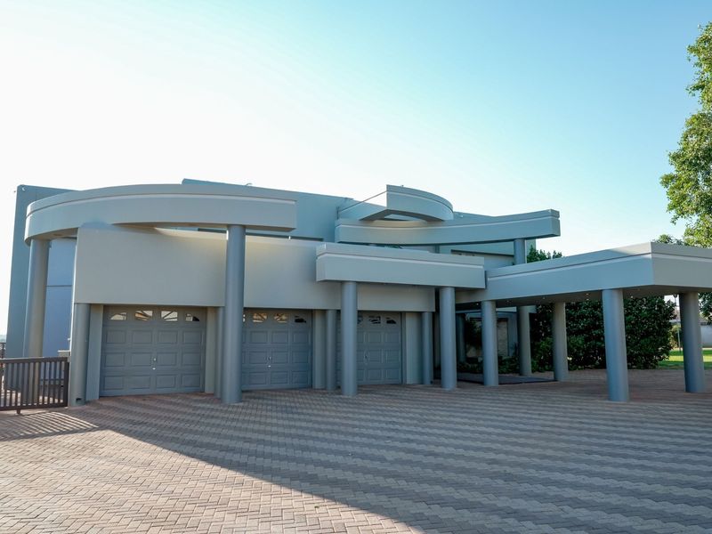 Modern architectural front facade featuring a triple garage, expansive paved driveway, and a prominent covered entrance with structural columns.