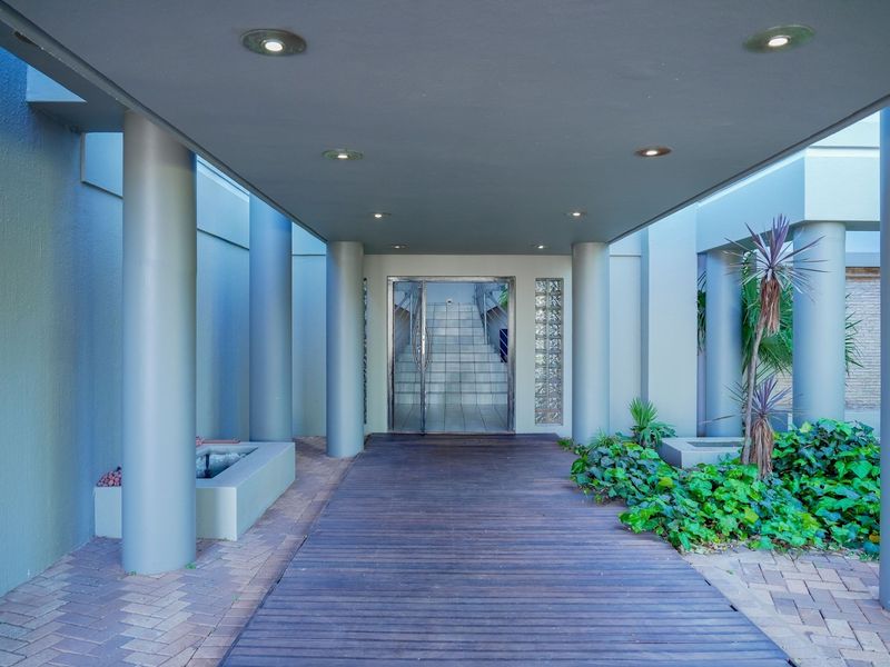 A modern covered entrance featuring a timber deck walkway, structural columns, and a glass door with decorative glass block side panels.
