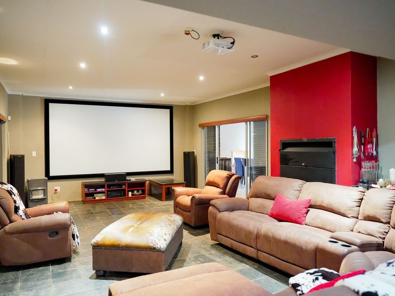 A dedicated cinema room featuring a large projection screen, ceiling-mounted projector, built-in fireplace, and tiled flooring with direct access to an adjoining space.