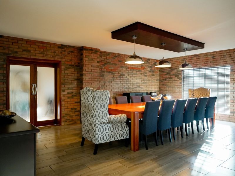Spacious dining room featuring exposed brick walls, tiled flooring, and a modern suspended bulkhead with pendant lighting, creating a warm and inviting atmosphere.