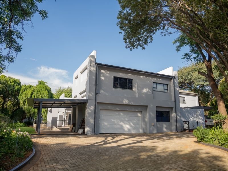 A modern double-story house featuring a paved driveway, a double garage with a sectional door, and an attached carport, set in a landscaped garden.