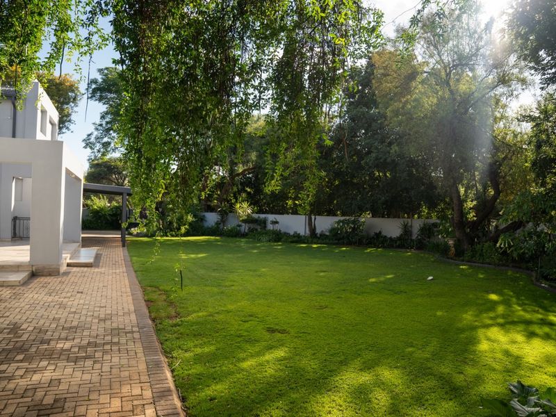 A spacious rear garden featuring a well-maintained lawn, paved patio area, and mature trees providing shade and privacy.