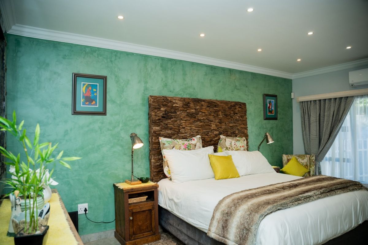A well-maintained bedroom featuring a textured green accent wall, recessed ceiling lighting, and a wall-mounted air conditioning unit.