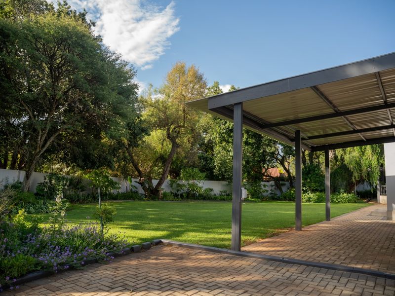 A spacious covered patio with paved flooring overlooking a well-maintained garden and lush green lawn.