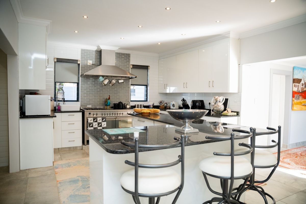 Modern kitchen featuring a central island with granite countertops, high-gloss cabinetry, a gas stove with stainless steel extractor fan, and stylish subway tile backsplash.