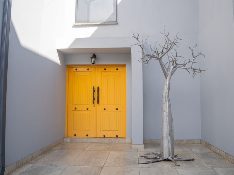 A bright entrance area featuring a bold yellow double front door, tiled flooring, and clean grey exterior walls.