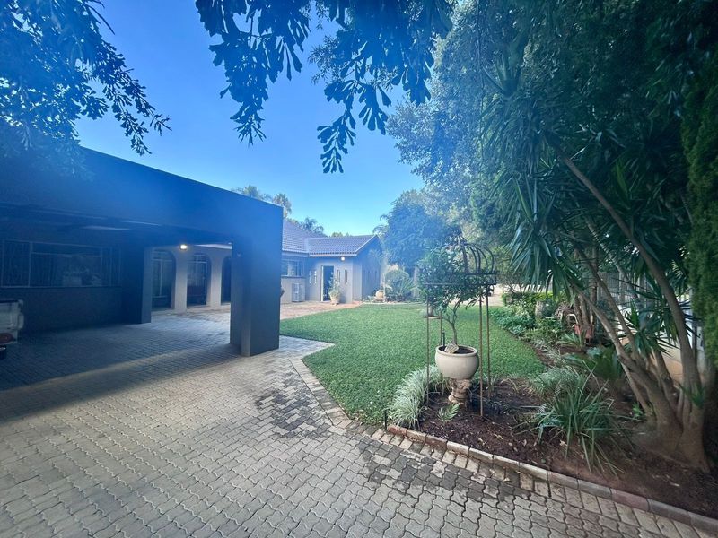 A well-maintained front exterior featuring a paved driveway, covered carport, and established garden area leading to the main house entrance.