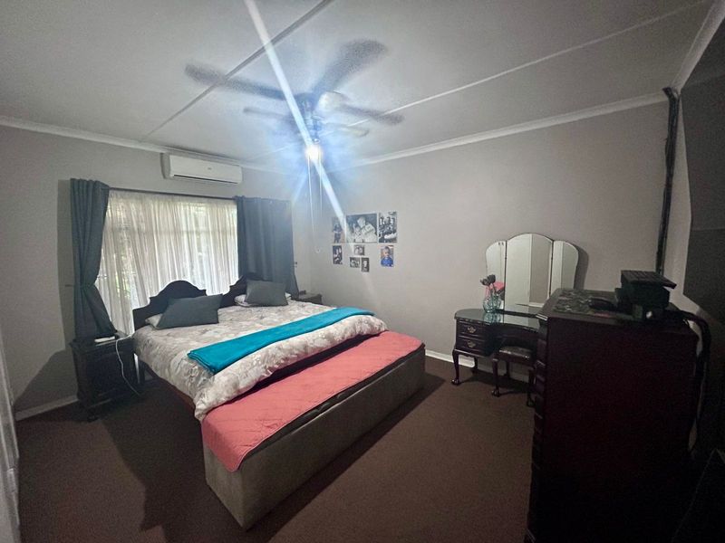 A spacious bedroom featuring carpeted flooring, a ceiling fan, and a wall-mounted split-system air conditioning unit.