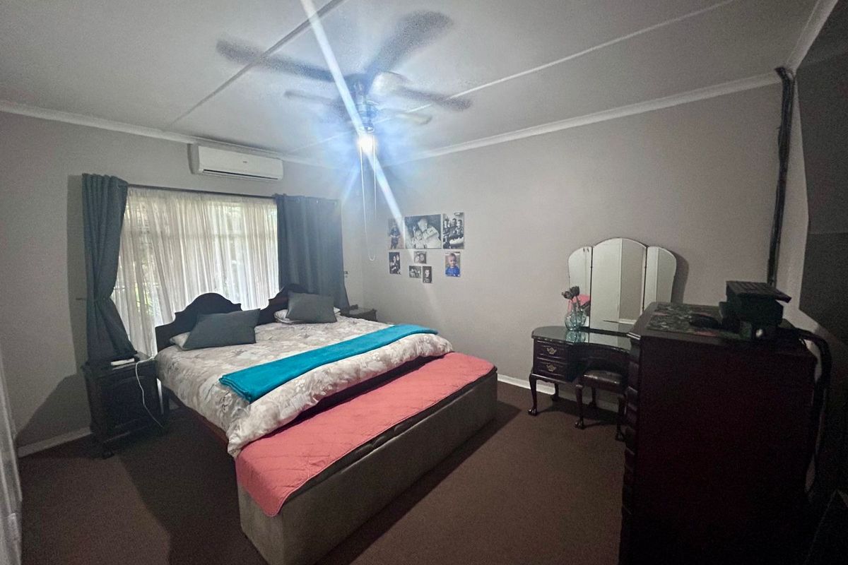 A spacious bedroom featuring carpeted flooring, a ceiling fan, and a wall-mounted split-system air conditioning unit.