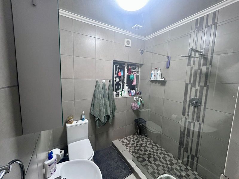 Modern bathroom featuring a walk-in shower with glass screen, mosaic floor tiling, neutral wall tiles, and functional sanitaryware.
