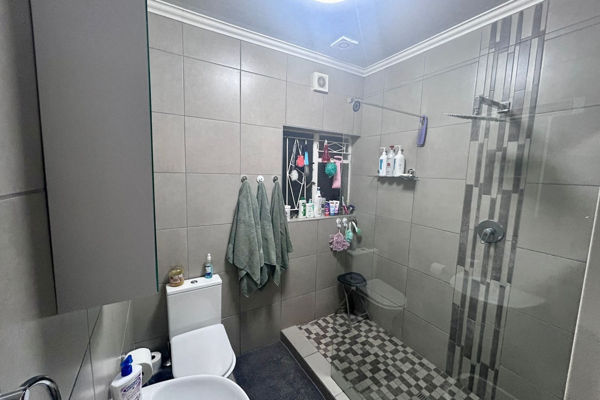 Modern bathroom featuring a walk-in shower with glass screen, mosaic floor tiling, neutral wall tiles, and functional sanitaryware.