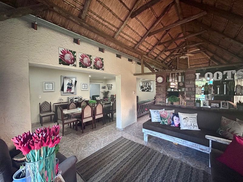 Spacious open-plan living and dining area featuring a high thatched roof with exposed timber trusses and a rustic brick feature wall.