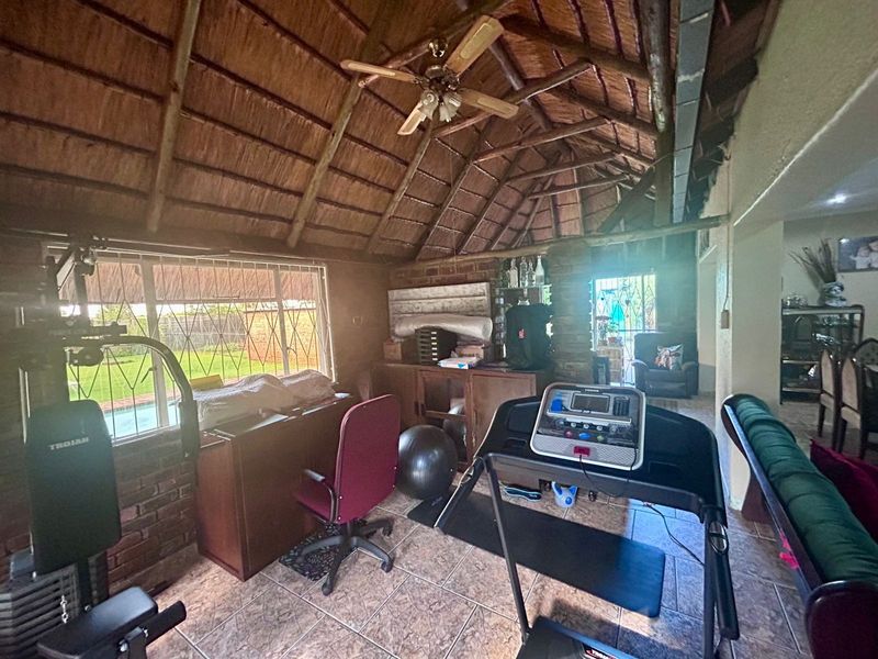 Spacious living area featuring a high thatched roof with exposed timber rafters, exposed brick walls, and tiled flooring, offering a rustic aesthetic.