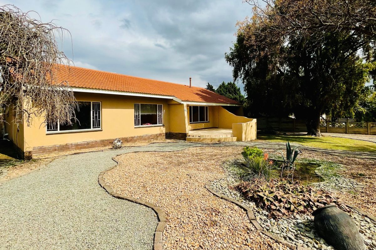Rear view of a single-story house featuring a terracotta tiled roof, plastered walls, a covered patio area, and a landscaped gravel garden.